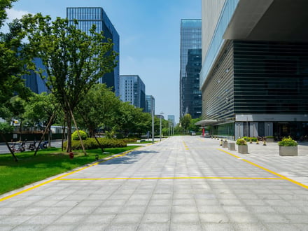 Modern business district plaza with glass towers and tree-lined walkway.