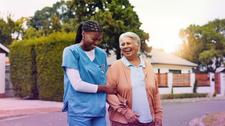 A caregiver walks with an elderly woman in a residential neighborhood.